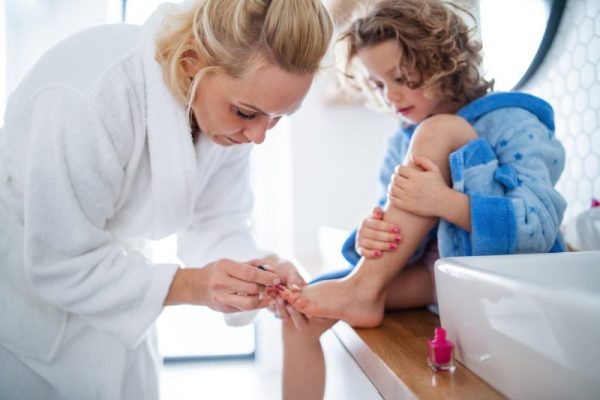 A cute small girl with mother in bathroom indoors at home, painting nails.