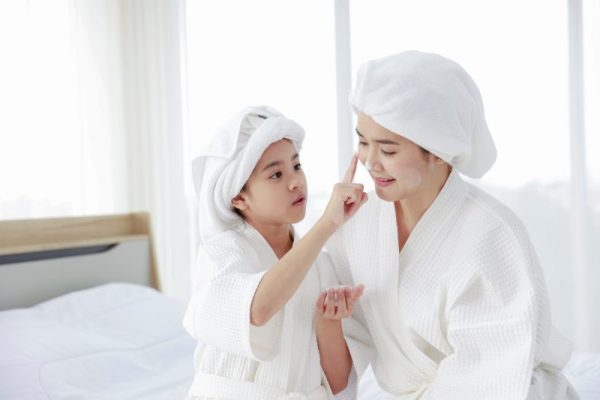 A young girl gently applies a facial mask to her mother’s face
