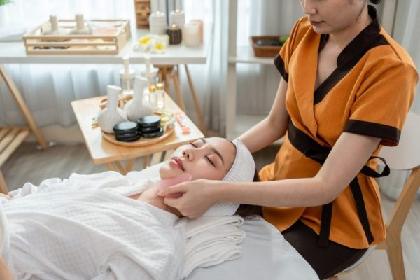 Asian young woman getting facial massage with gua sha at beauty spa.