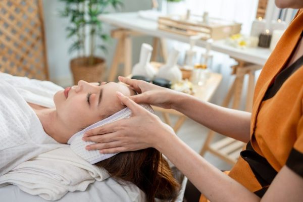 Asian young woman getting head and facial massage treatment at beauty spa.