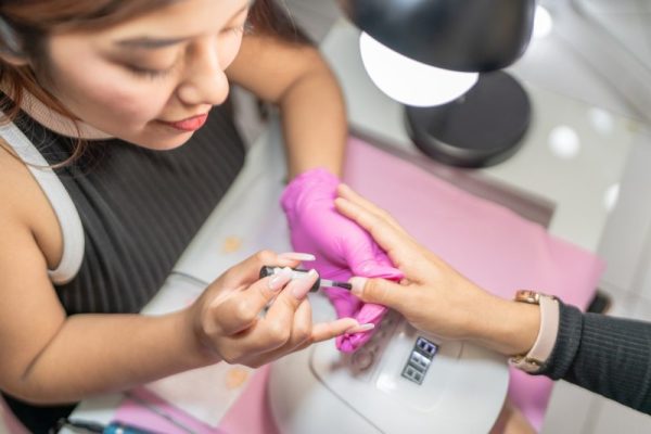 Beautician applying nail polish to woman's fingernails in beauty salon