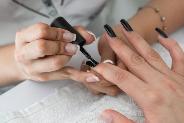 close-up detail shot of a manicurist's hands painting the nails with a black nail polish