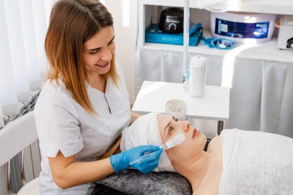 Hands of cosmetology specialist applying gold facial mask using brush