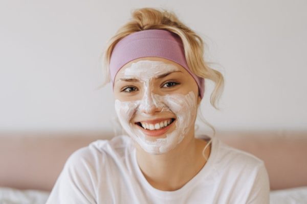 Happy young girl with facial clay mask staying at home, looking at camera