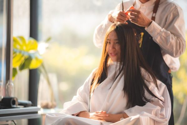 Young woman getting hair cut and hair styling done in modern salon by professional barber